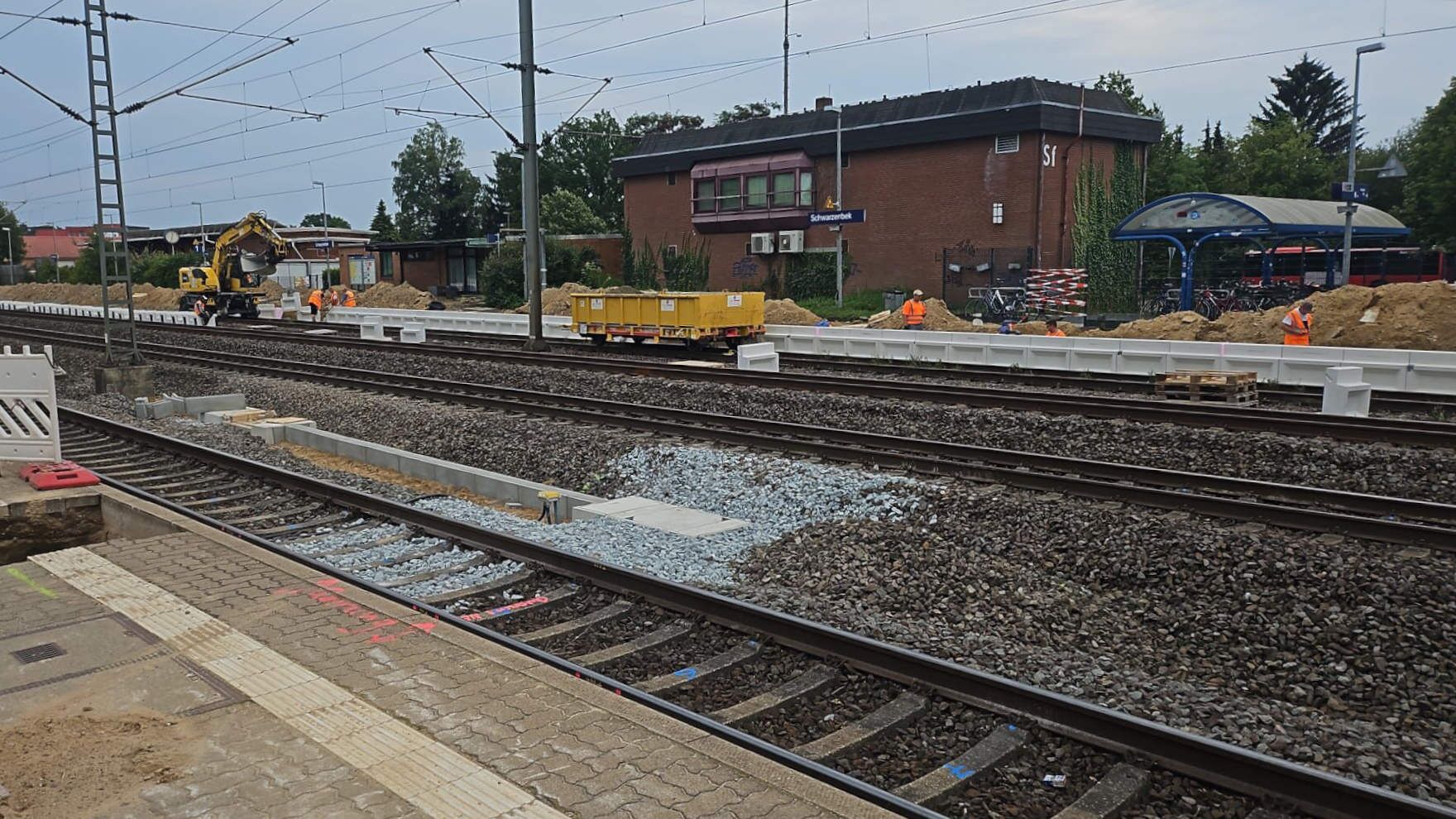 Das Gleisfeld im Bahnhof Schwarzenbek. Ein Zwei-Wege-Bagger fährt über die Gleise, davor steht ein Güterwagen. (Foto: DB InfraGO AG)